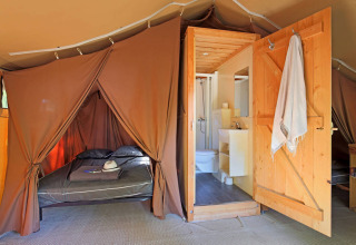 Interior photo of a Toile&Bois tent Sweet safari tent showing a bed, bathroom, and wooden door.