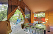 Interior de una tienda safari Toile&Bois tent Sweet con mesa, sillas y vista exterior a los árboles.