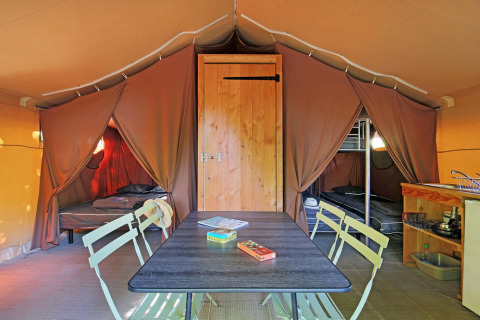 Interno di una tenda safari Toile&Bois tent Sweet con tavolo da pranzo, due camere e angolo cottura.