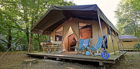 Toile&Bois Safari Tent Sweet met houten terras, stoelen en tafel buiten, omgeven door groene bomen.