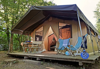 Tente safari Sweet Toile&Bois avec terrasse en bois, chaises et table à l'extérieur, entourée d'arbres.