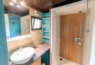Baño moderno en Chalet Evasion glamping con lavabo redondo, ducha de madera y estantes azules.