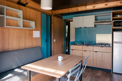 Moderne indretning i Chalet Evasion glamping, med tekøkken, spisebord og sofa i lyse træfarver.
