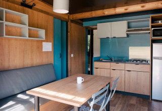 Moderne indretning i Chalet Evasion glamping, med tekøkken, spisebord og sofa i lyse træfarver.