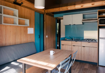 Moderne indretning i Chalet Evasion glamping, med tekøkken, spisebord og sofa i lyse træfarver.