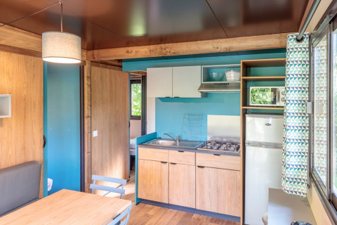 Cocina moderna en alojamiento glamping Chalet Evasion con acabados de madera, estufa y ventana grande.