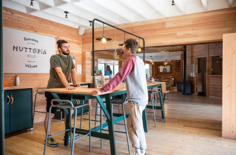 Two men conversing at the wooden reception area in Village Huttopia Lac de Rillé holiday park, France.