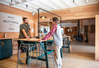Two men conversing at the wooden reception area in Village Huttopia Lac de Rillé holiday park, France.
