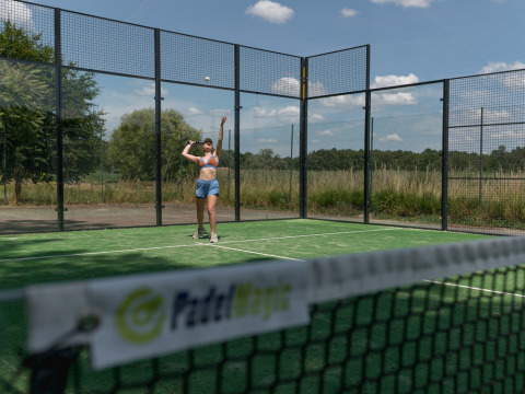 Eine Frau spielt Padel auf einem Außenplatz im Village Huttopia Lac de Rillé in Centre-Val de Loire, Frankreich.