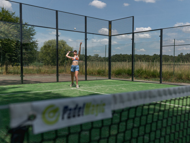 A woman plays padel on an outdoor court at Village Huttopia Lac de Rillé, Centre-Val de Loire, France.