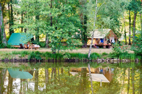 Campingplads ved søen i Village Huttopia Lac de Rillé, Centre-Val de Loire, Frankrig, omgivet af skov.