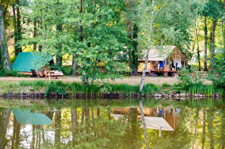 Lakeside camping scene at Village Huttopia Lac de Rillé, Centre-Val de Loire, France, with tents and trees.