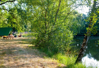 Camping by the lake with green trees at Huttopia Lac de Rillé, Centre-Val de Loire, France.