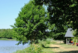 Rustig meer met groene bomen en vakantiehuisjes aan het water, Village Huttopia Lac de Rillé, Frankrijk.