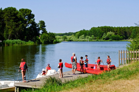 Niños y adultos con chalecos salvavidas disfrutan actividades acuáticas en el lago de Village Huttopia Lac de Rillé.