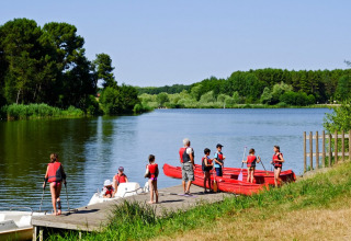 Children and adults in life jackets prepare for boating on a lake at Village Huttopia Lac de Rillé in France.