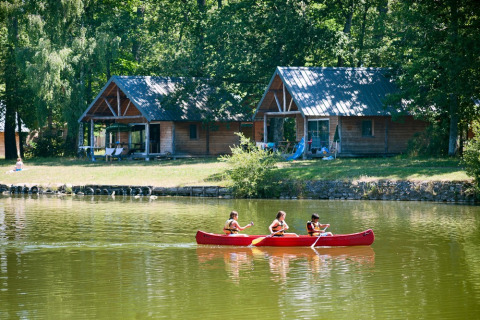 Kinderen varen in een kano op het meer bij houten chalets in Village Huttopia Lac de Rillé, Loire.