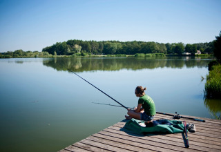Persona che pesca su un molo di legno al lago nel Village Huttopia Lac de Rillé, Centre-Val de Loire, Francia.