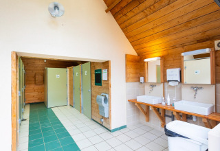 Sauberes, helles Badezimmer mit grünen und weißen Fliesen, zwei Waschbecken, Spiegeln und Toilettenkabinen.