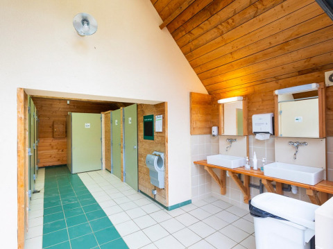 Baño luminoso y limpio con azulejos verdes y blancos, dos lavabos, espejos y varias cabinas de inodoro.