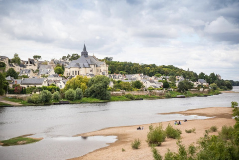 Panoramaudsigt over en landsby ved floden med en kirke i centrum og folk på sandstranden i Centre-Val de Loire.