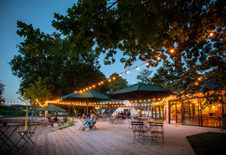 Udendørs terrasse med lyst kæde, parasoller og borde i feriebyen Village Huttopia Lac de Rillé, Frankrig.