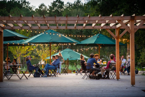 Outdoor dining area at Village Huttopia Lac de Rillé, guests seated under green umbrellas with string lights.