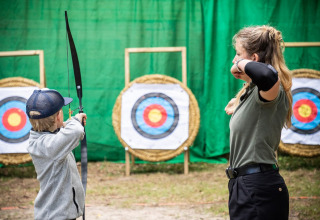 En kvinde og et barn øver bueskydning mod mål i ferieparken Village Huttopia Lac de Rillé i Frankrig.