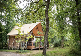 Houten chalet met terras te midden van bomen bij Village Huttopia Lac de Rillé, Centre-Val de Loire, Frankrijk.