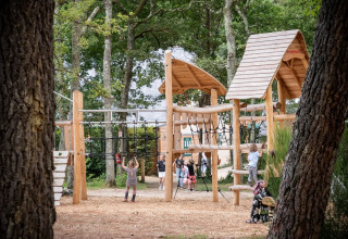 Kinderen spelen op een houten speeltuin in het bos bij Village Huttopia Lac de Rillé in Frankrijk.
