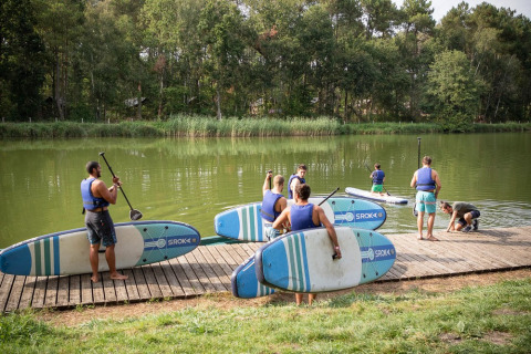 Huéspedes del parque vacacional con chalecos salvavidas preparándose para hacer paddle surf en Lac de Rillé, Francia.