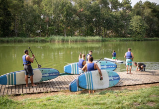 Vakantieparkbezoekers met zwemvesten bereiden zich voor op stand-up paddleboarding aan Lac de Rillé, Frankrijk.