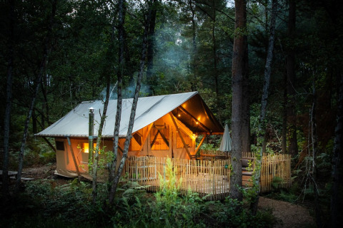 Tienda de glamping iluminada al atardecer en el bosque de Village Huttopia Lac de Rillé, Centre-Val de Loire, Francia.