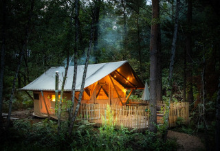 Verlicht glamping tent tussen de bomen in Village Huttopia Lac de Rillé, Centre-Val de Loire, Frankrijk, bij valavond.