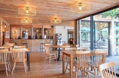 Interior luminoso de restaurante con muebles de madera y ventanales en Village Huttopia Lac de Rillé, Francia.