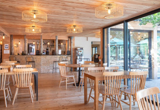Lyst og moderne restaurantinteriør med træmøbler og store vinduer i Village Huttopia Lac de Rillé, Frankrig.