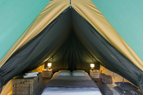 Interior de una tienda tipi con cama, mesitas, lámparas y bolsas, mostrando un ambiente acogedor.