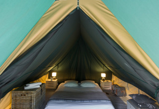 Interior de una tienda tipi con cama, mesitas, lámparas y bolsas, mostrando un ambiente acogedor.