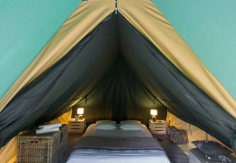 Interior de una tienda tipi con cama, mesitas, lámparas y bolsas, mostrando un ambiente acogedor.