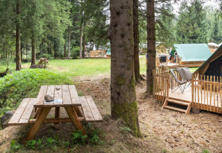 Tienda tipi sobre plataforma de madera en el bosque, con mesa de picnic y arroyo cercano, ideal.