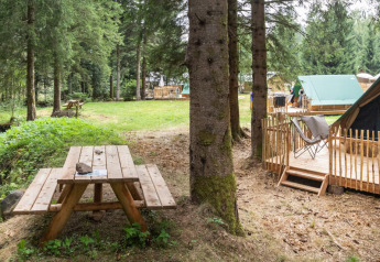 Tienda tipi sobre plataforma de madera en el bosque, con mesa de picnic y arroyo cercano, ideal.