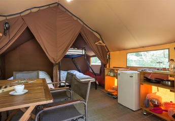 Innenansicht eines gemütlichen Canadienne-Safari-Zeltes mit Betten, Küchenecke und Esstisch in Huttopia Lac de Rillé.