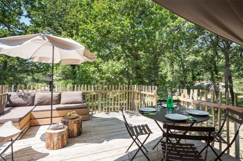 Terrasse extérieure du lodge Canadienne au Village Huttopia Lac de Rillé, France, avec coin repas et salon.