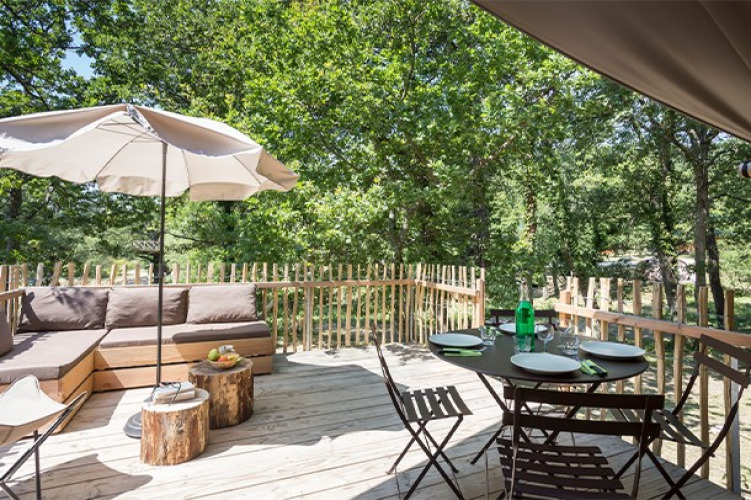 Terraza al aire libre en la tienda safari Canadienne en Village Huttopia Lac de Rillé, Francia, con mesa y sillas.
