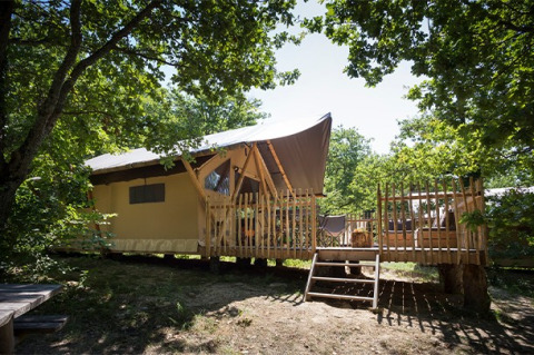 Canadienne safari tent with wooden deck among trees, perfect for a comfortable and scenic camping retreat.