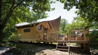 Canadienne safaritent met houten terras in een bosrijke omgeving, ideaal voor een unieke kampeerervaring.