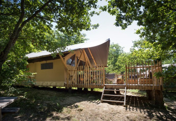 Tente safari Canadienne avec terrasse en bois sous les arbres, parfaite pour un séjour de glamping en nature.