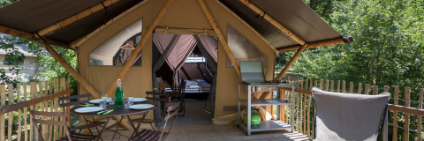 Tente safari avec terrasse, table extérieure, barbecue et vue sur la forêt. Hébergement glamping moderne.