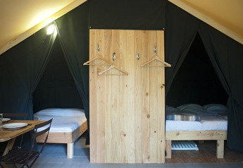 Interieur van een safaritent met twee bedden, houten scheidingswand en eettafel met servies.