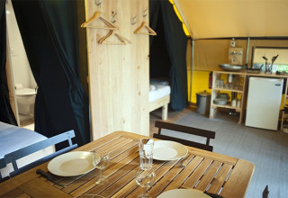 Vista interna di una tenda safari con tavolo da pranzo, angolo cucina, letti e bagno visibile.